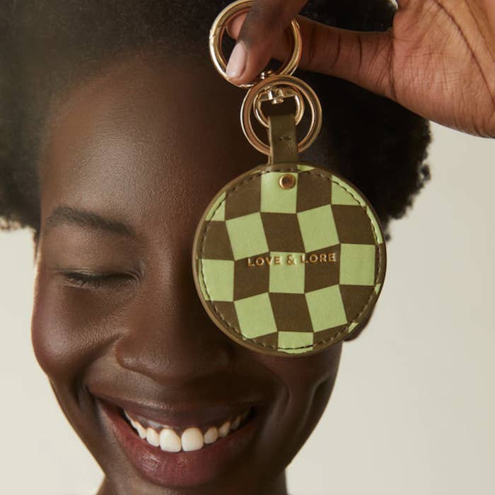 a smiling person holding the keyring with hidden mirror up to their face