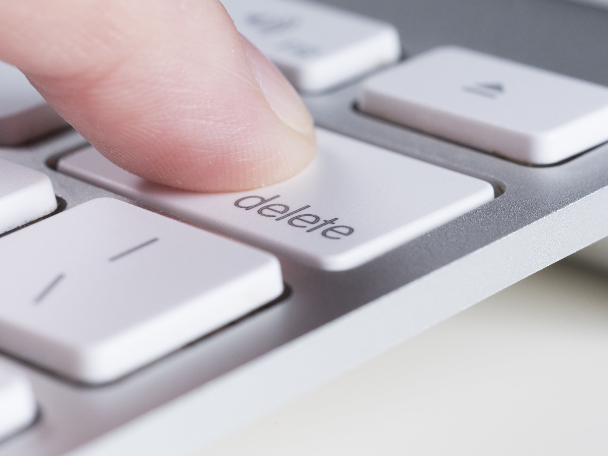A finger presses the delete key on a computer