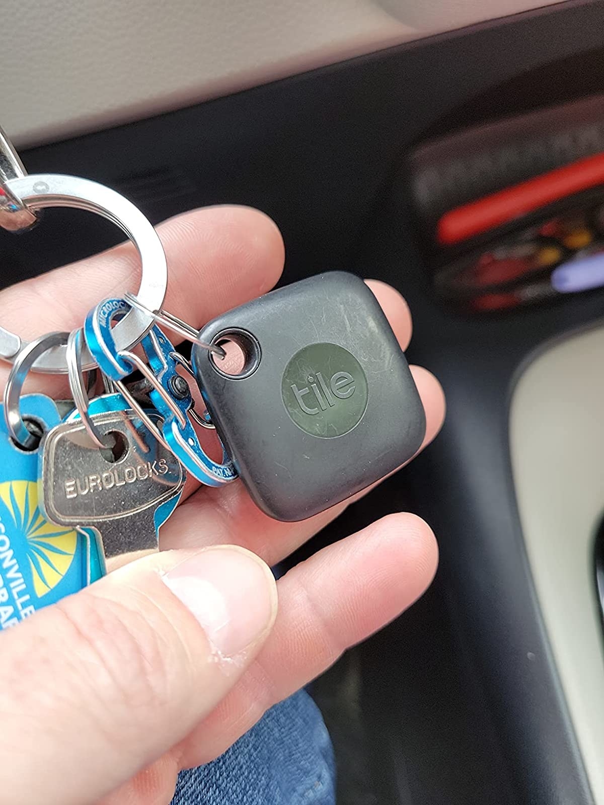 Reviewer holding their keys with the bluetooth Tile tracker attached