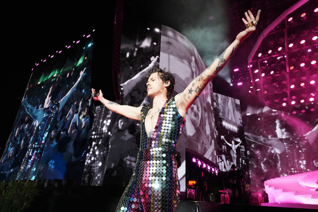 Harry in a sequined bodysuit onstage with his arms outstretched