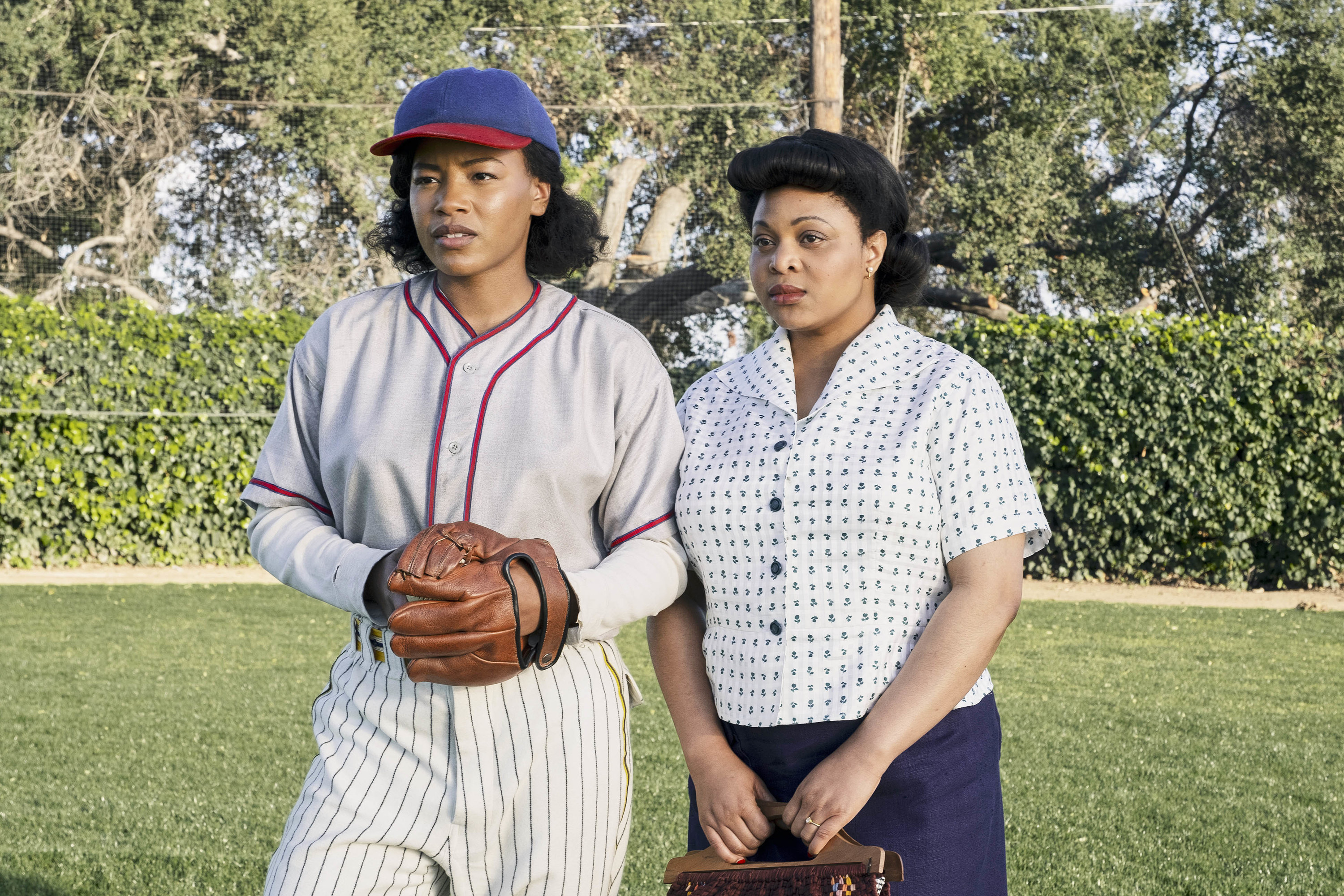 Two black women standing next to each other while one is in a baseball uniform