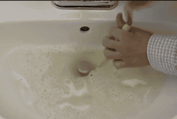 a person using the drain snake to unclog a sink