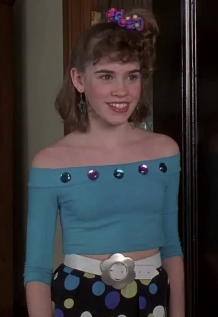 Christa smiling and wearing a three-quarter-sleeve, off-the-shoulder top and a hair tie