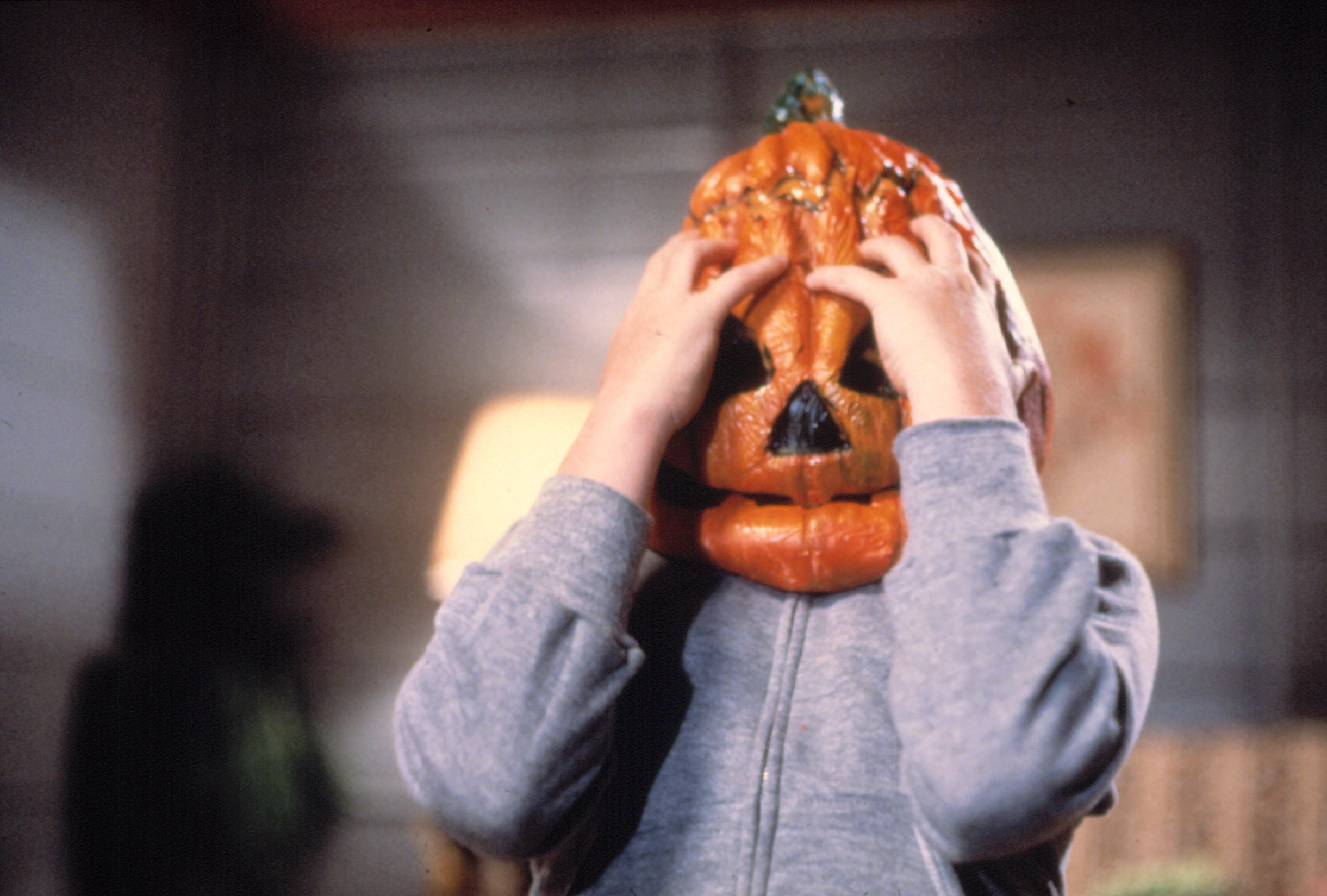 A small child wearing a melting pumpkin mask
