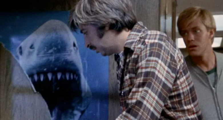 Two men stand in front of a Jaws poster