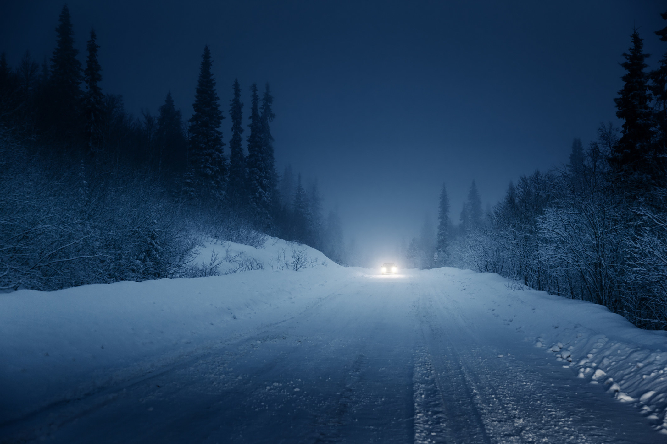 a snowy road with headlights in the distance