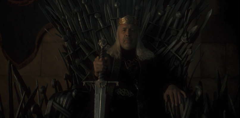 Viserys sitting on the Iron Throne while holding a sword