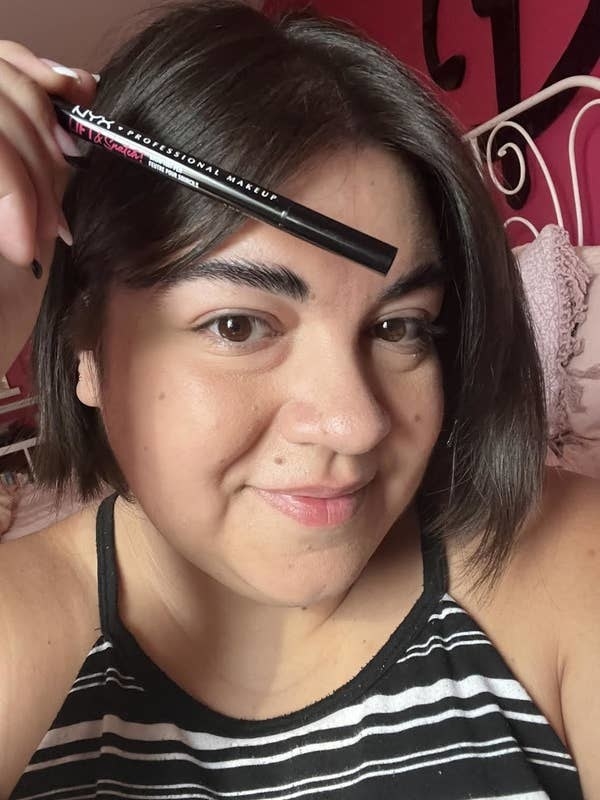 a person holding up a nyx brow pen next to their eyebrows