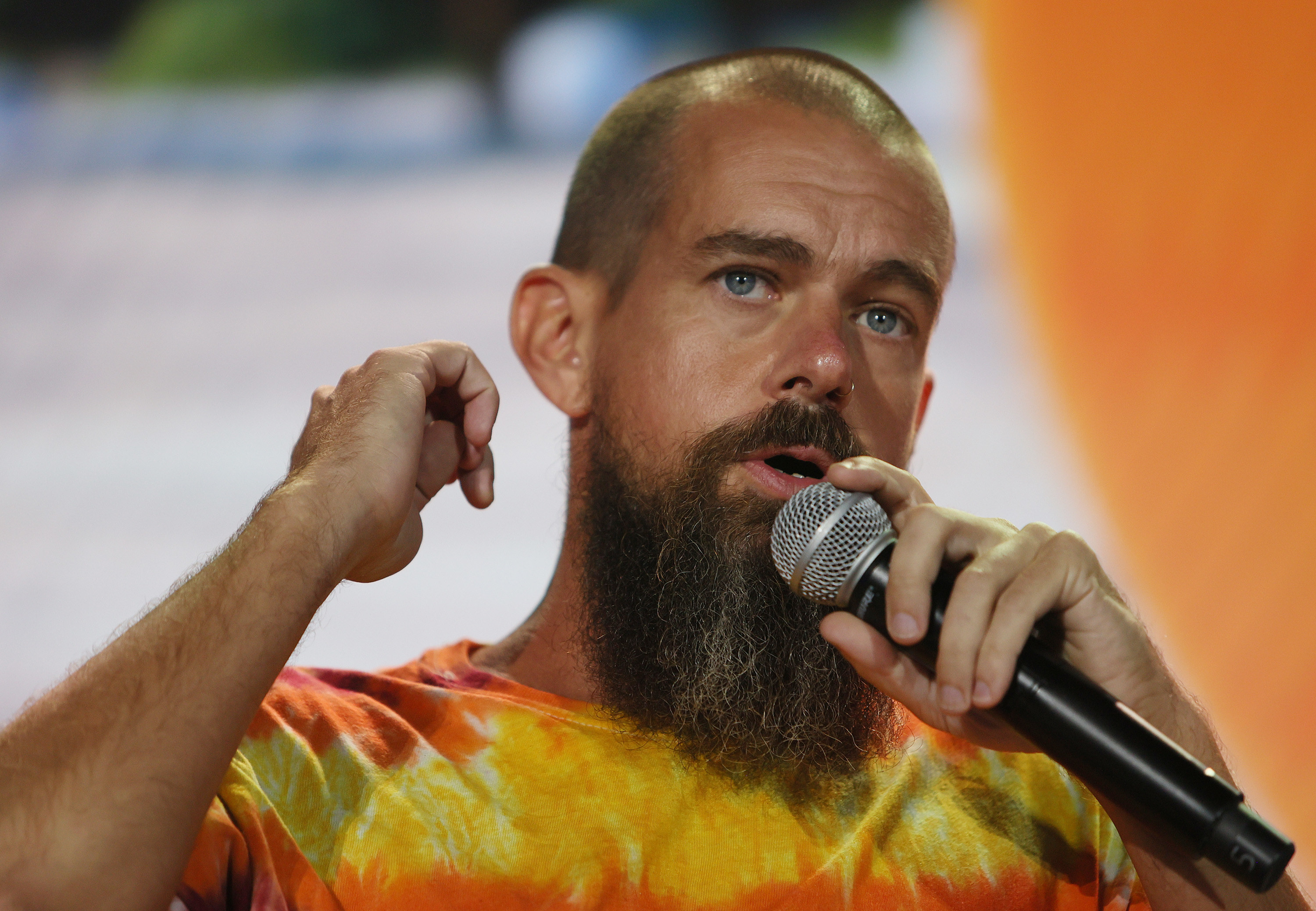 jack dorsey in an extensive beard and tie dye shirt holds a microphone