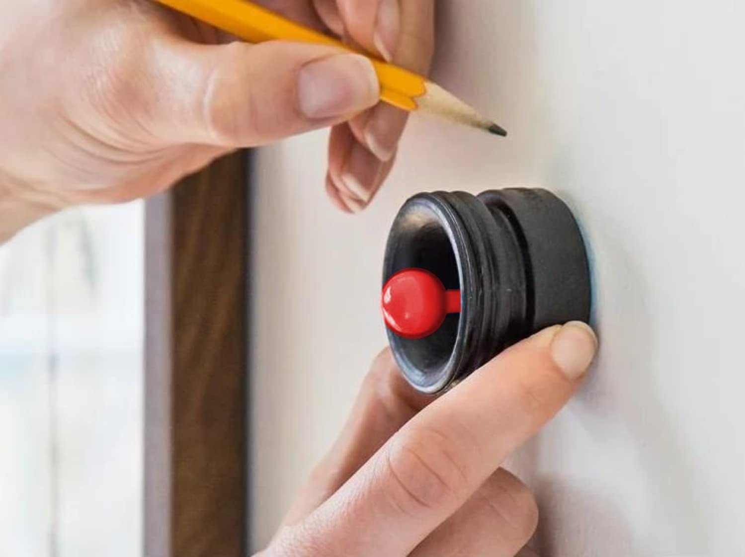 hand using the small round tool with red knob against a wall