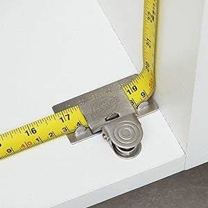 metal clip holding measuring tape so it can bend up a wall