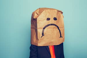 person with paper bag over their head with a sad face on the bag