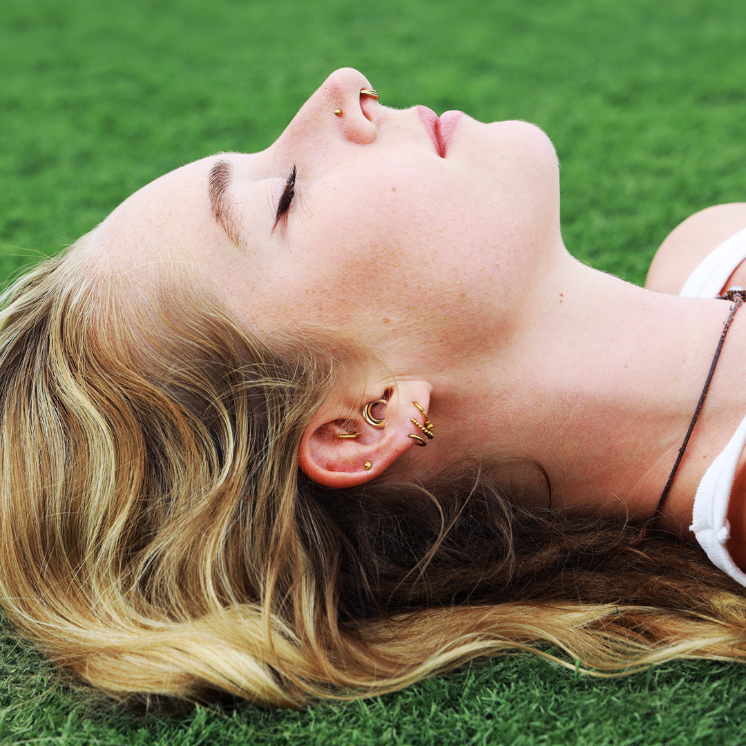 a person lying on the grass while wearing the gold ear plugs