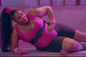 Lizzo lays on a yoga mat wearing a leotard over biker shorts