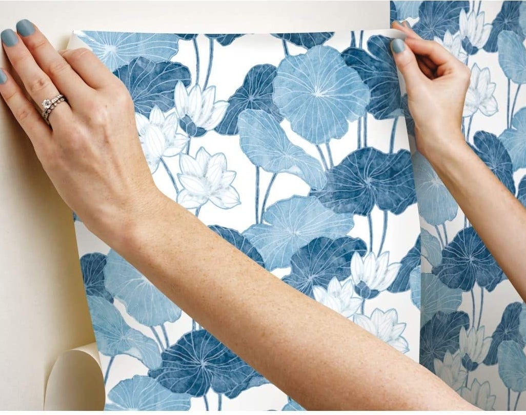 A person applying the wallpaper to their wall