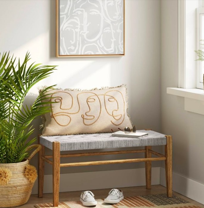 Woven bench with a pillow on it, next to a floor plant