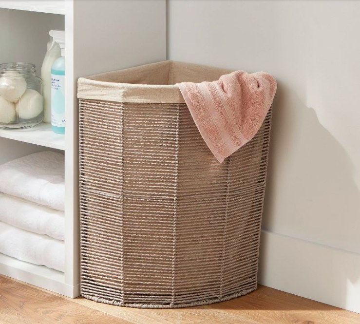 Laundry basket in a corner with a pink towel draped over the top