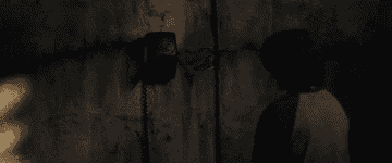 A GIF of Finney from behind, as he answers a black phone on the wall of a dark and dingy basement then turns to face the camera