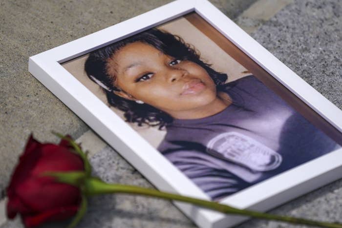 A photo of Breonna Taylor in a photo frame sits on the ground with a rose placed on top
