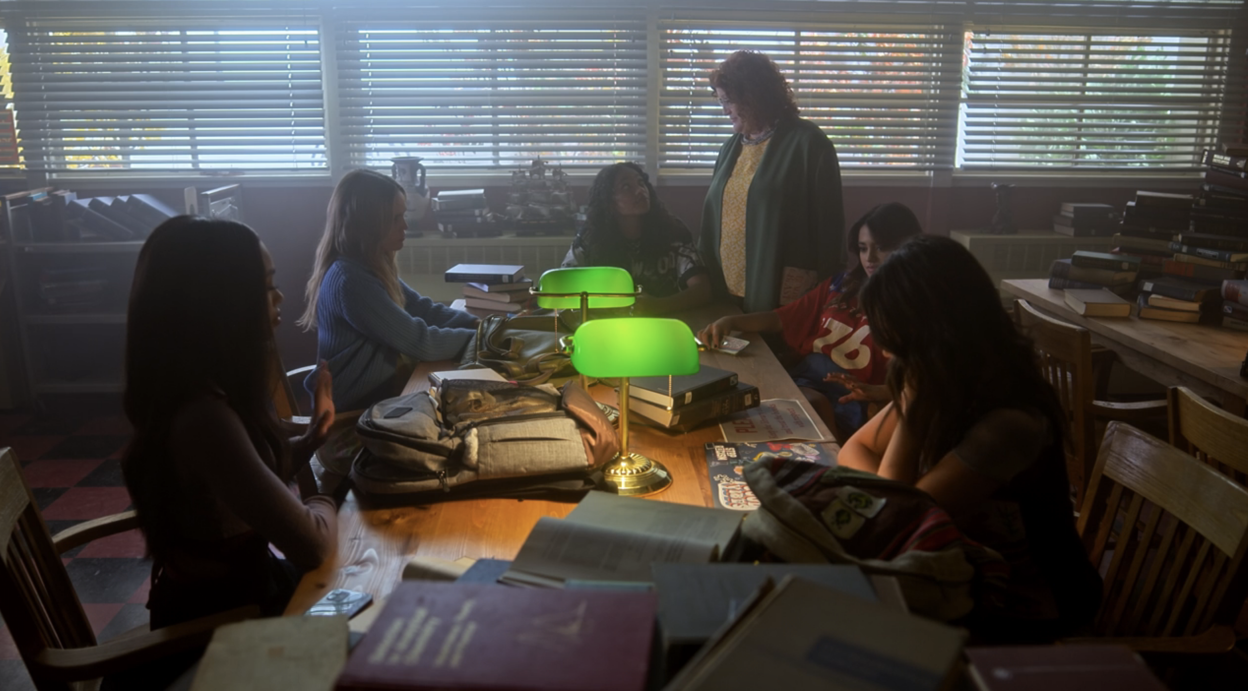 The Liars sitting in a classroom around a table with books on it