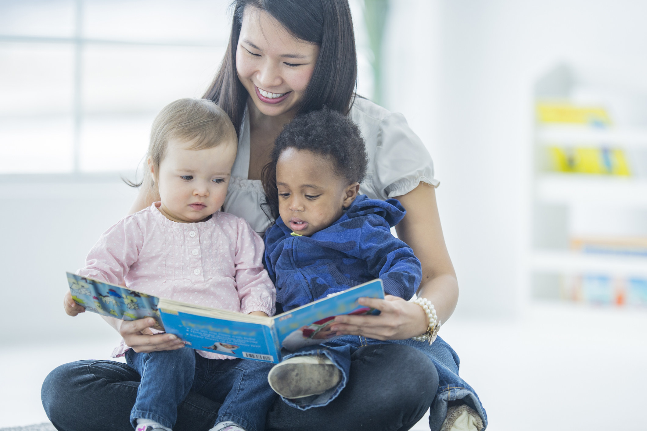 Woman with two toddler on her lap as she reads them a book