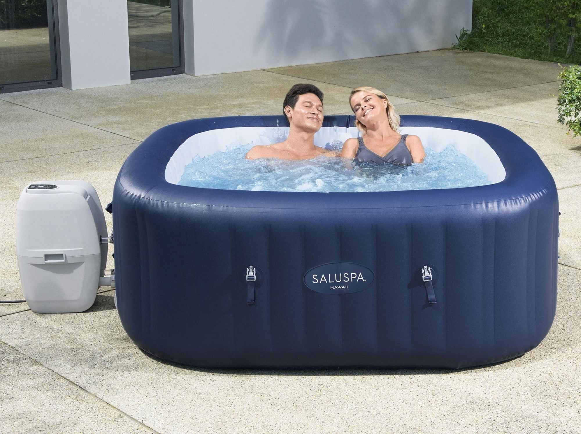 a couple sitting in the blue hot tub in a backyard