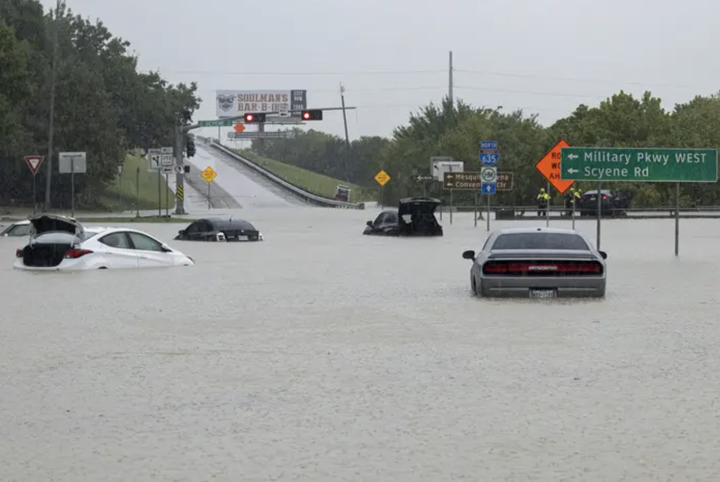 A freeway overpass filled with water on a grey day, cars are submerged in the water
