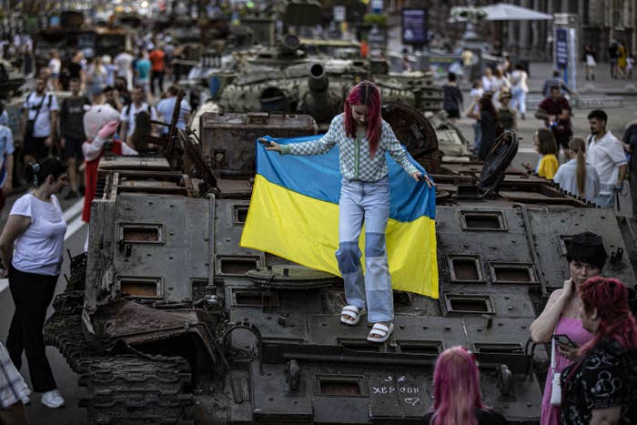 a young girl with pink hair holding the ukrainian flag stands on a captured russian tank in downtown kyiv