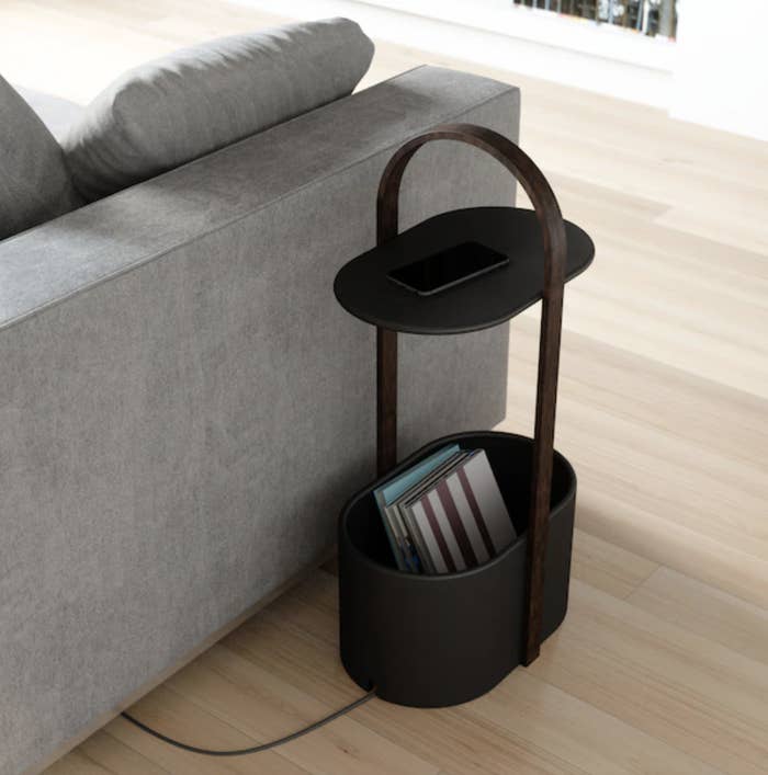 an oval-shaped side table with slots for charging cables and a large bottom basket filled with books