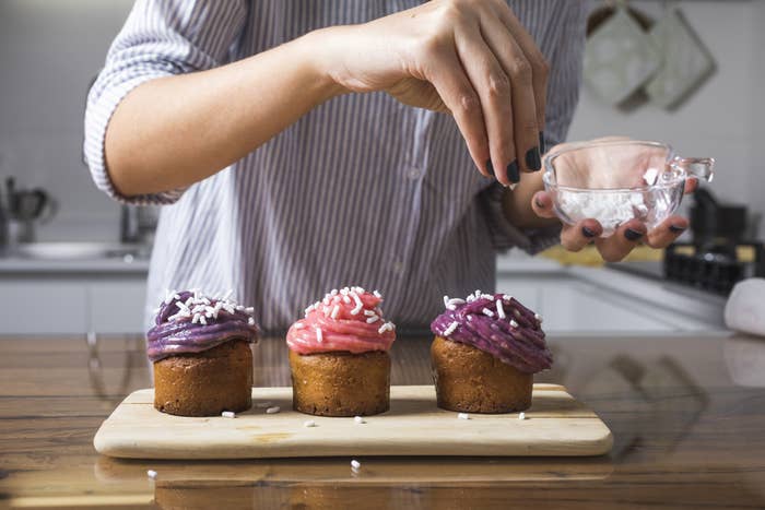 hands pouring sprinkles on cupcakes