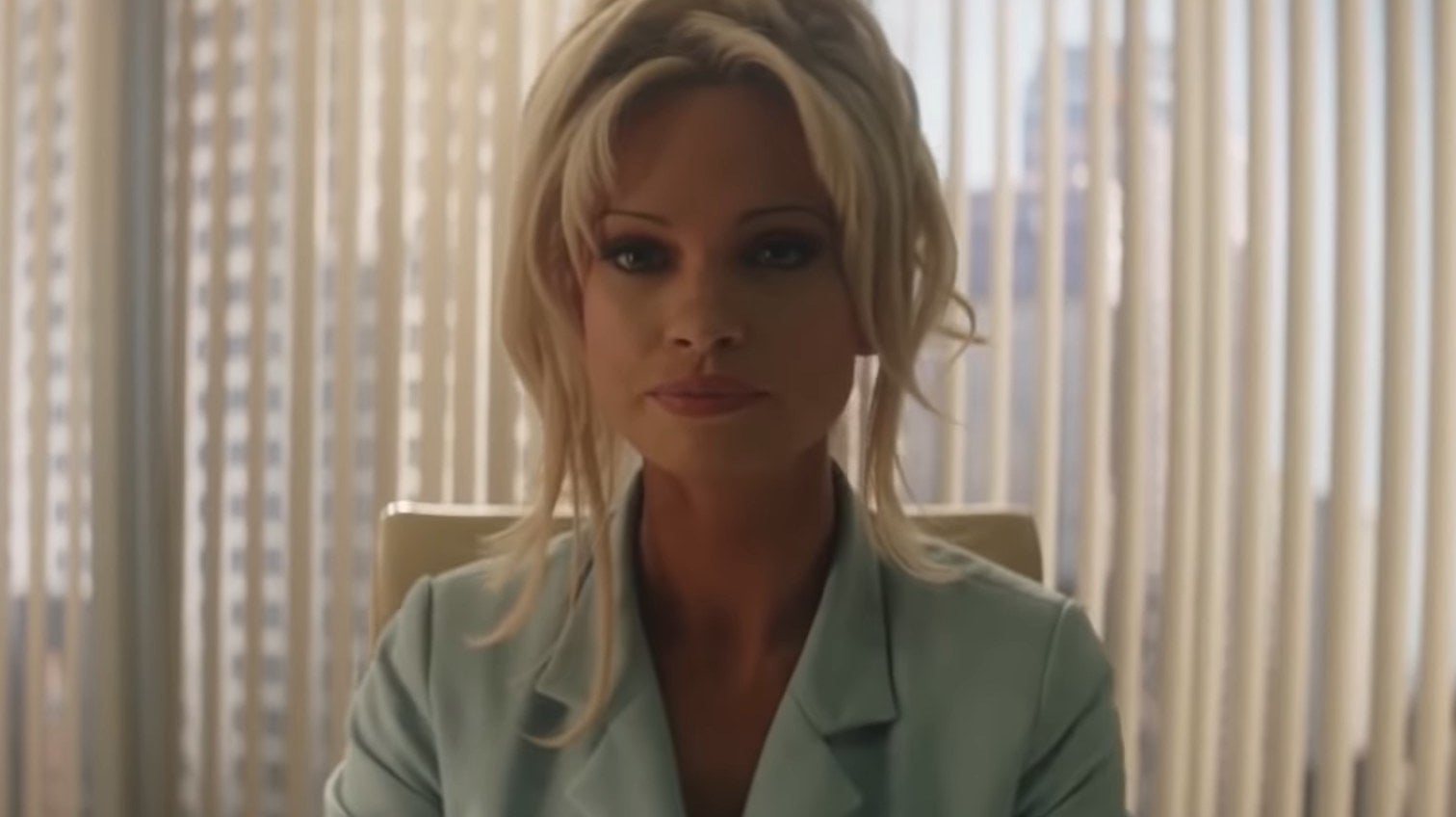 Pamela Anderson sitting in an office in &quot;Pam &amp; Tommy&quot;
