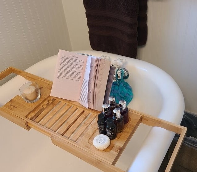 reviewer photo of the caddy on a tub with a book and bath supplies on it