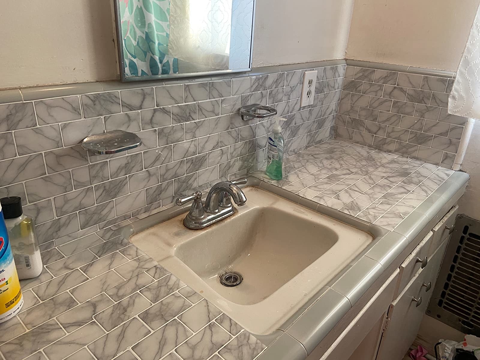 Reviewer&#x27;s bathroom vanity and sink are shown with the peel and stick tiles