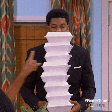 A GIF of a man holding a huge stack of styrofoam takeout containers