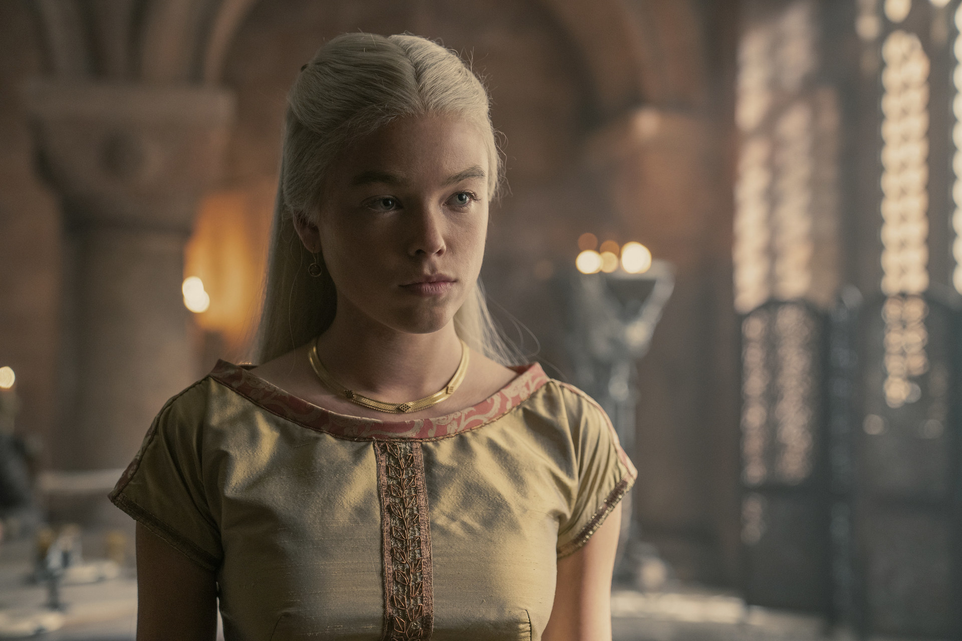 Rhaenyra Targaryen wears a gold gown and stands in the palace