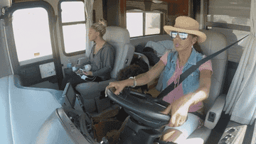 Two women are in a RV, the one driving is pumping her fist
