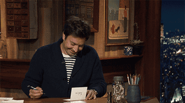 Jimmy Fallon writing a letter and laughing