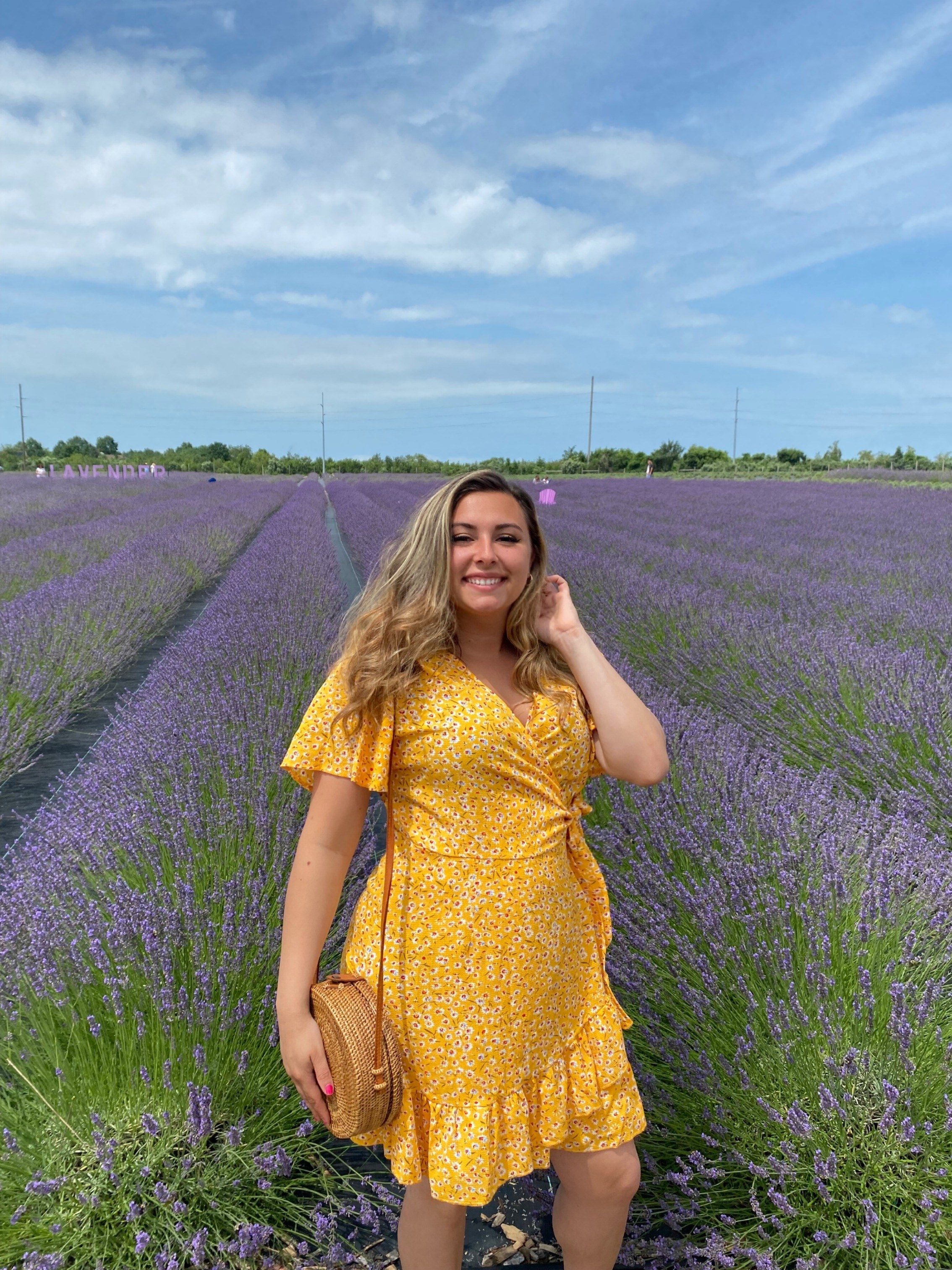 Reviewer standing in lilac field in  the yellow floral wrap dress