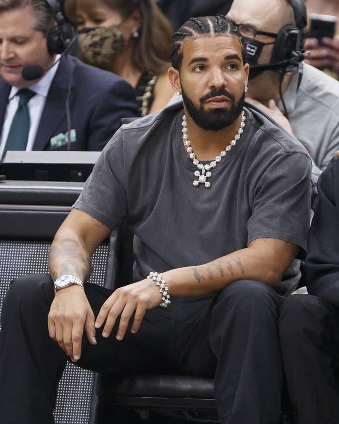 Drake sitting in the audience of a sports event, wearing braids