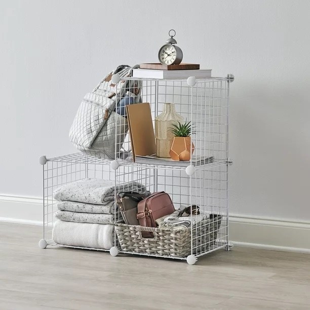 A white stackable cube unit full of grey blankets, a grey container with bags and room decor