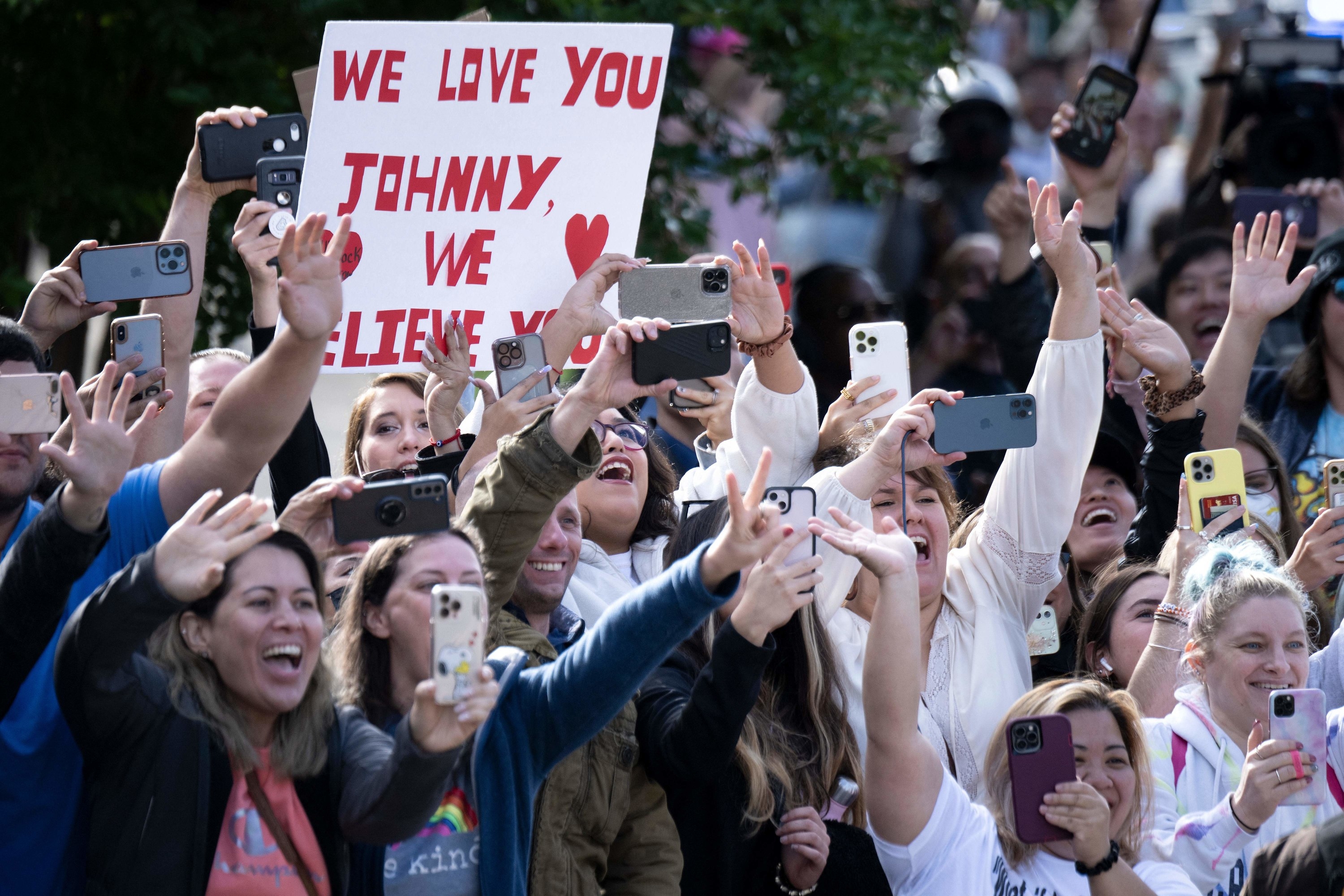 A throng of fans have their phones out to take pictures, with one holding up a sign that says &quot;We love you Johnny, we believe you&quot;