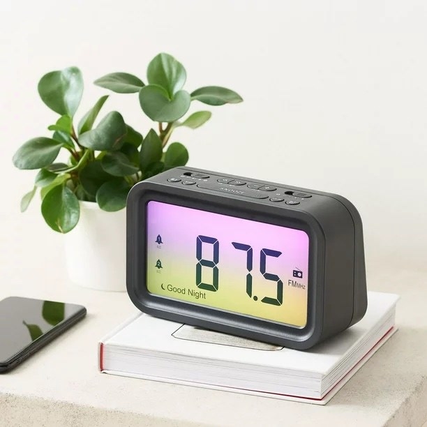 An alarm clock on a desk with an ombre background that goes from pink to yellow