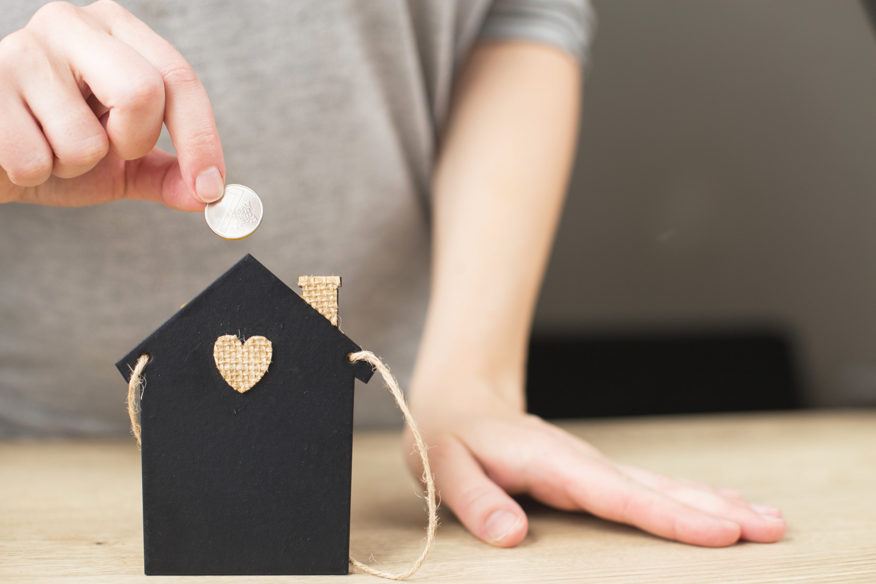 person putting coins into a house-shaped piggy bank