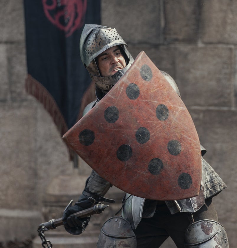 Criston Cole wears armor and holds up his shield mid-fight at a tourney