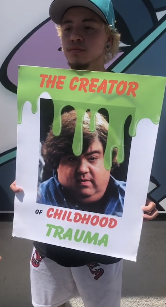 a protester holding a sign with Dan&#x27;s face being slimed as a face of childhood trauma