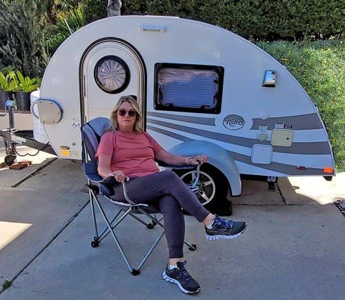 Reviewer lounging in the chair with legs crossed, sitting outside camper