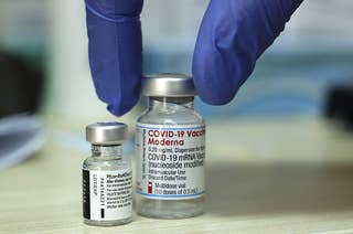 A medic places two vials of COVID-19 coronavirus vaccines on a table. The bottles are labeled Pfizer-BioNTech and Moderna.
