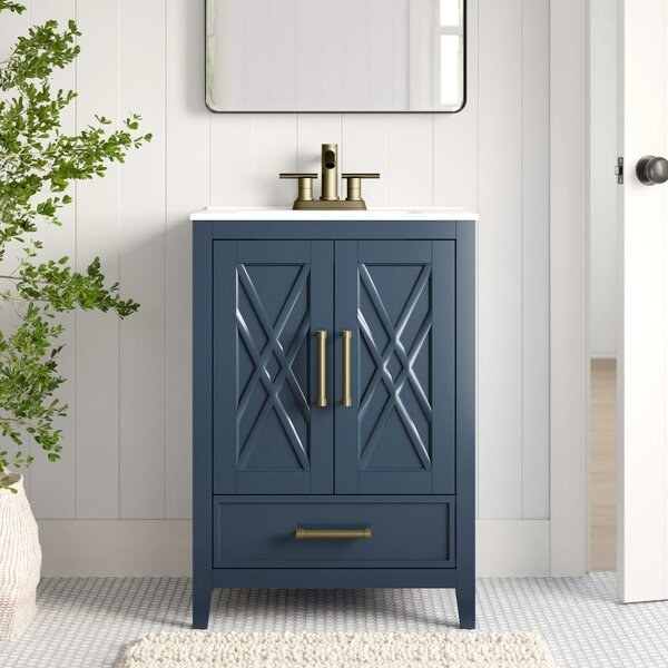 dark blue vanity and sink with an X crossed front detail on its two cabinets, a drawer under the cabinets, and gold bar hardware