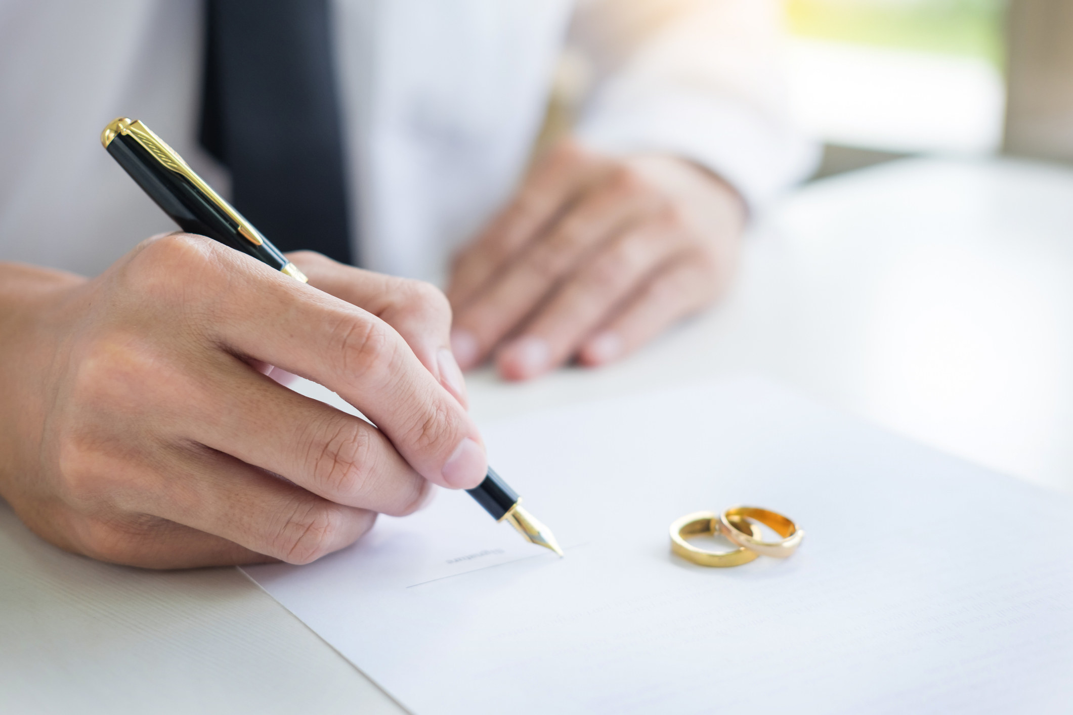 a person signing a document that has wedding rings sitting on it