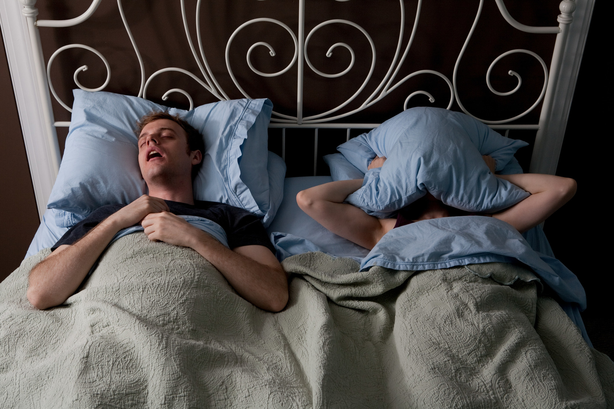 a person snoring and his partner with a pillow over their head